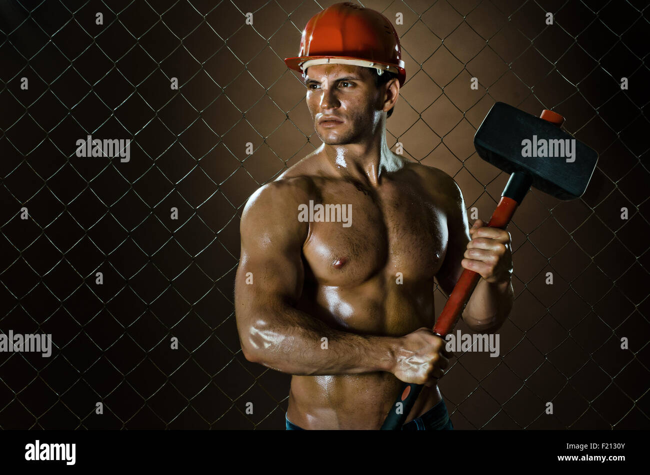 Lavoratore muscolare , nel casco di sicurezza con grande tup in mani, sulla compensazione sfondo di recinzione Foto Stock