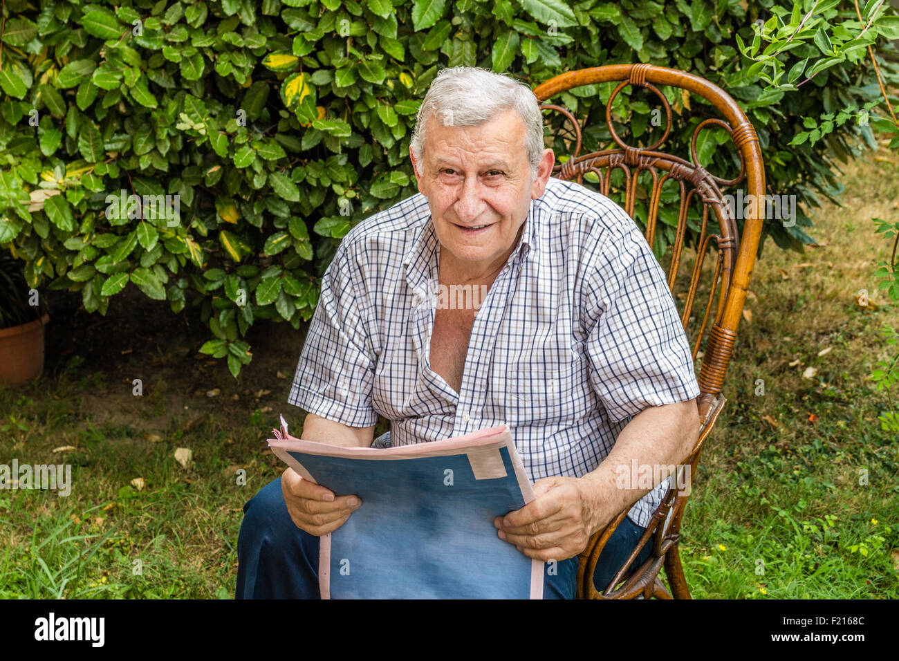 Tranquilla pensione, vecchio uomo legge il giornale in giardino Foto Stock