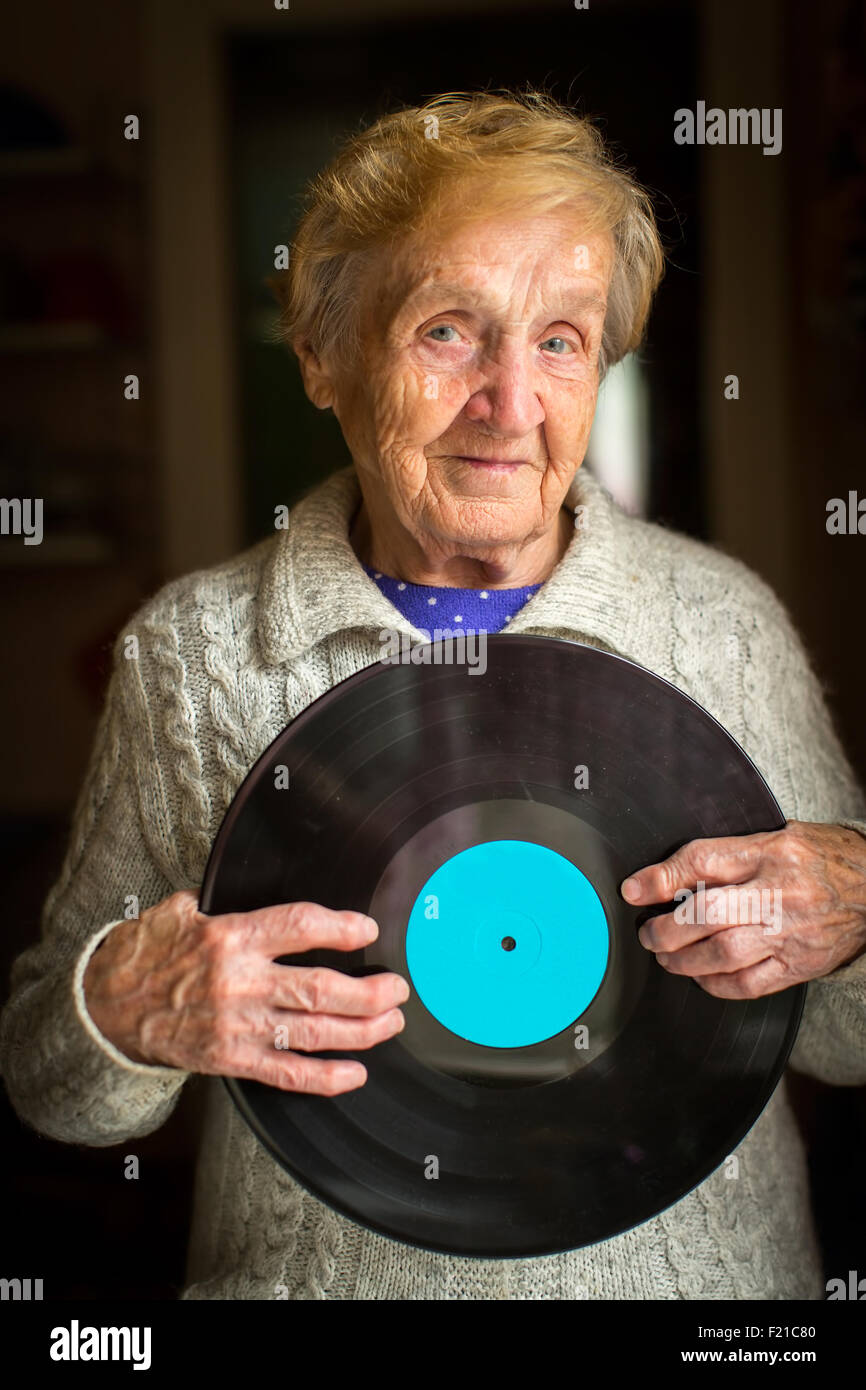 Vecchia donna sorge nella casa che tiene il record di vinile nelle sue mani. Foto Stock