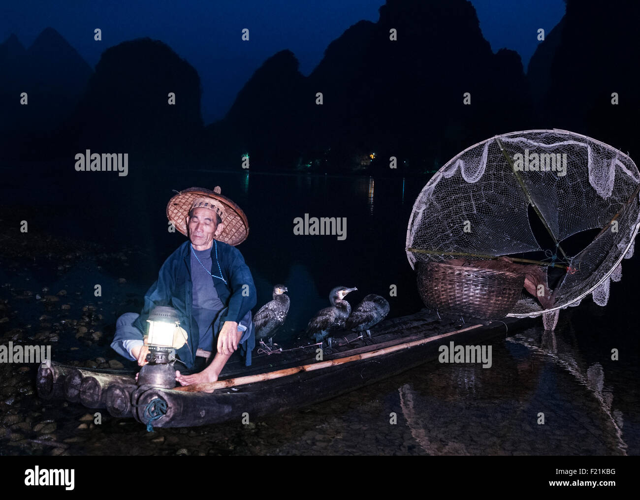 Cormorano Pescatore sul fiume Li di notte con circolare bianco net e i suoi uccelli per il recupero di pesce, Yangshuo, Cina e Asia Foto Stock