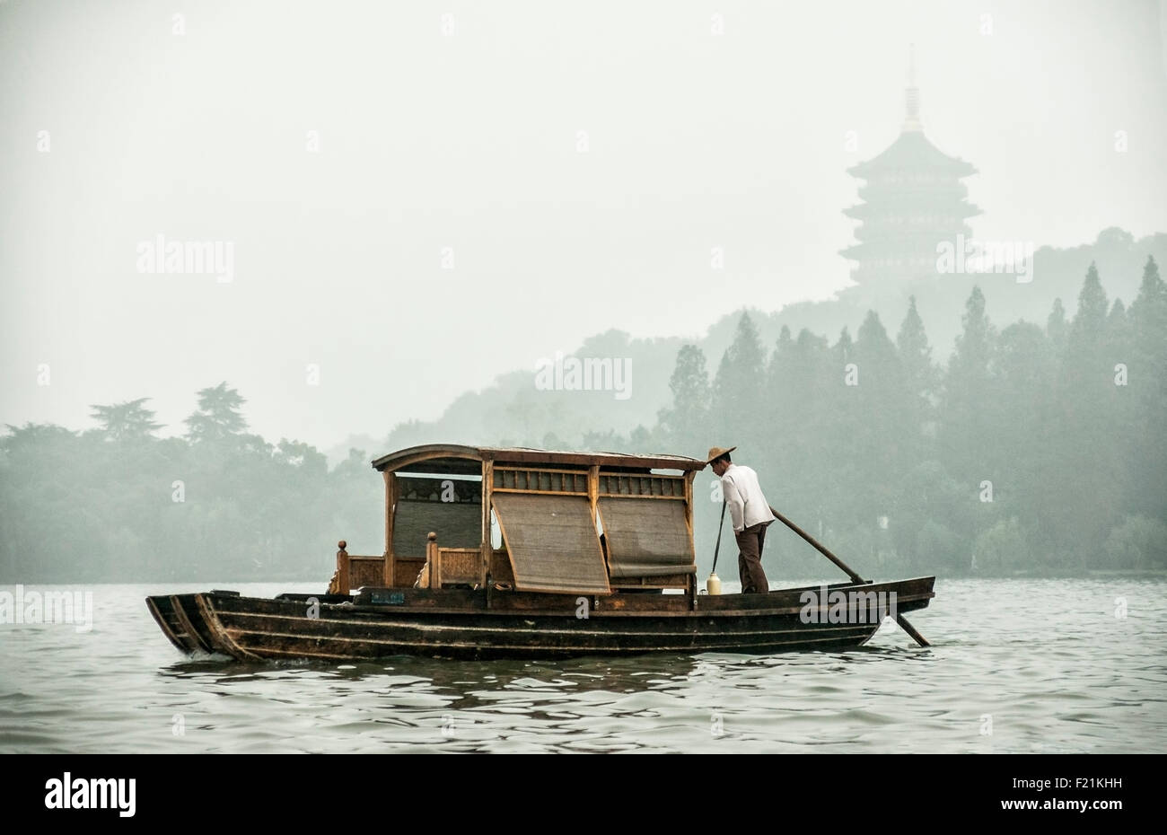 Uomo asiatico pagaie un rustico flottante in barca sul lago ovest su un nebbioso giorno, Hangzhou, Cina e Asia Foto Stock