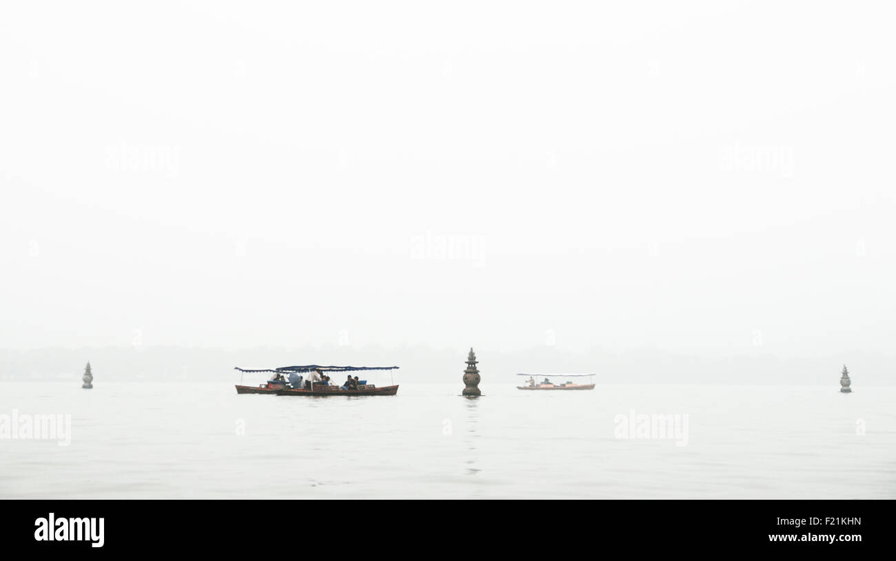 I turisti facendo una gita in barca sul Lago Ovest flottazione tra le tre pagode di pietra che salgono dal acqua su un nebbioso giorno, Hangzhou Foto Stock