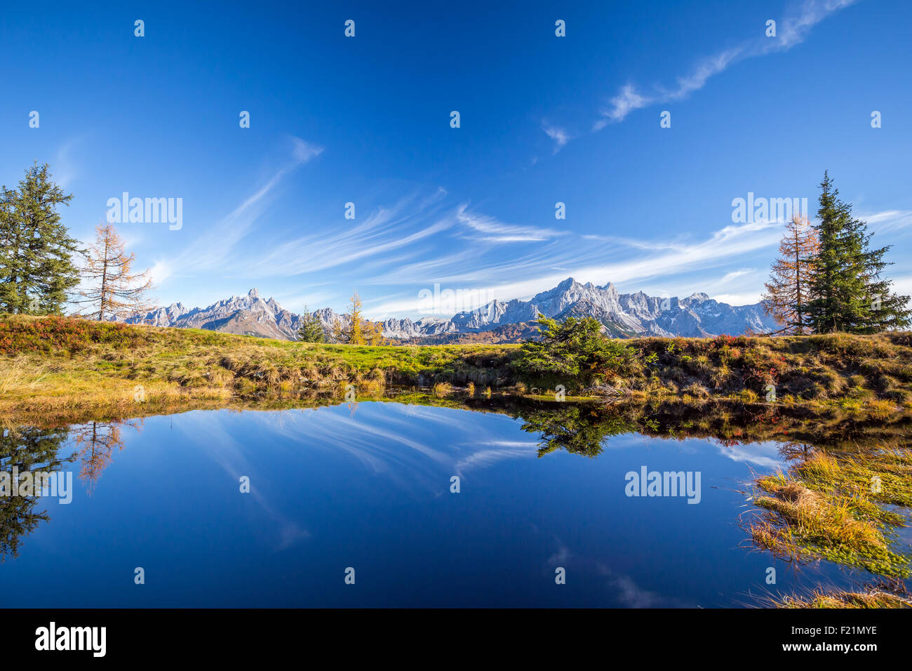 Un piccolo laghetto di montagna con picchi di montagna in background riflette il blu del cielo Foto Stock