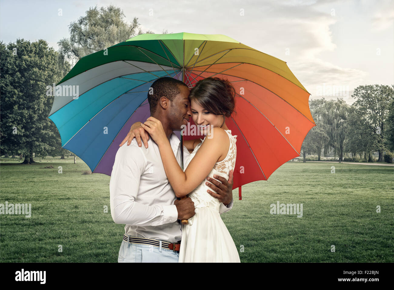 Mezzo Corpo colpo di un dolce coppia giovane sotto un ombrello coloratissimo in una piovosa foggy park Foto Stock