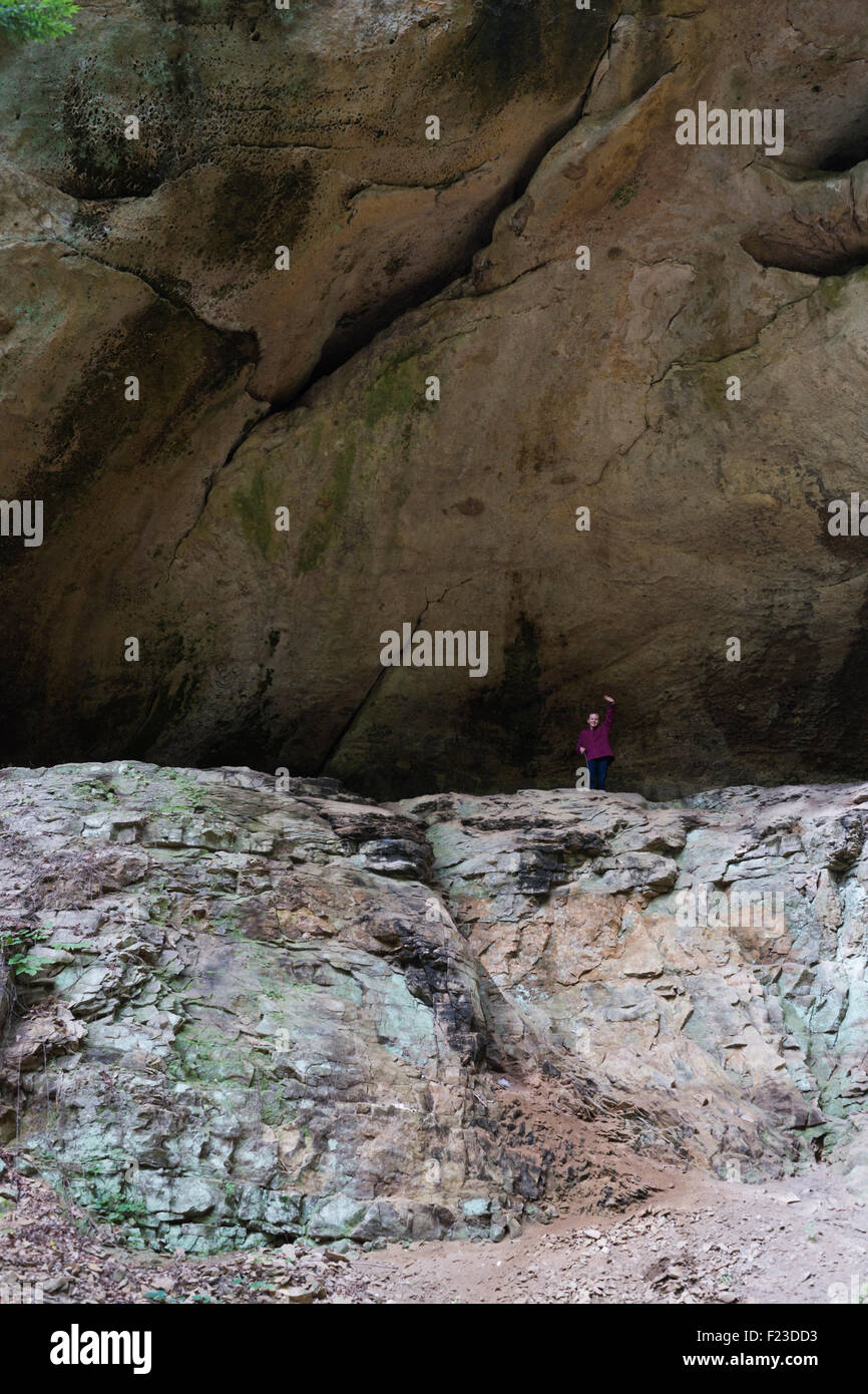 Ragazza e permanente fino ad arrivare a toccare enorme roccia sporgenza su scogliere Hemlock trail, Hoosier National Forest, inglese, Indiana Foto Stock
