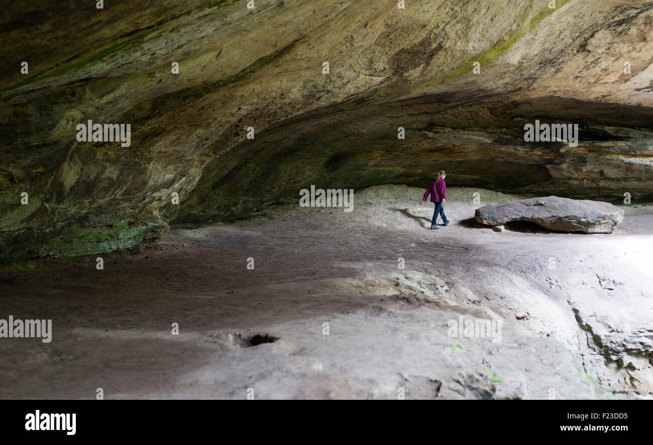 Ragazza camminare sotto una grande roccia a sbalzo la cicuta scogliere, Hoosier National Forest, inglese, Indiana Foto Stock