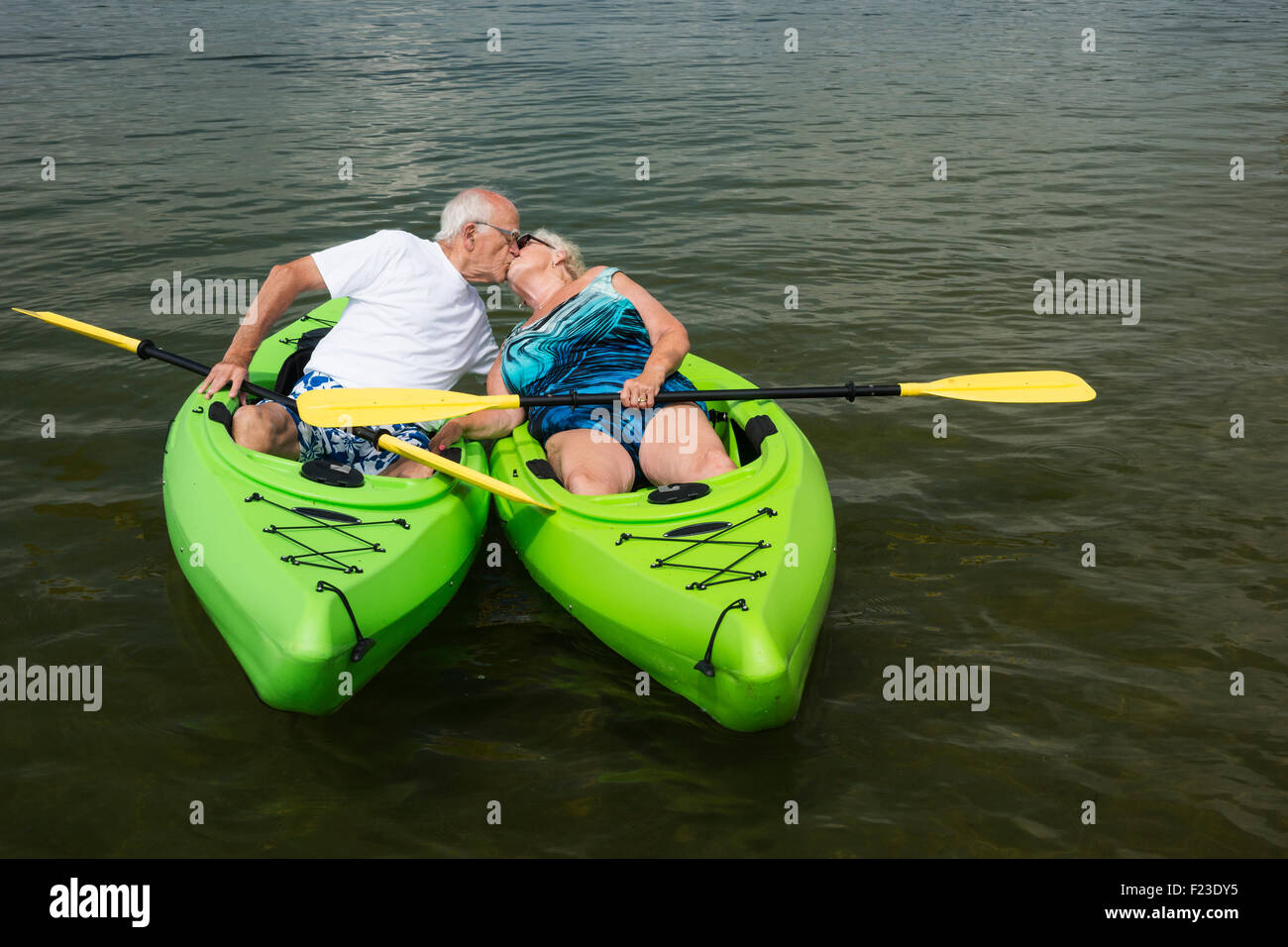 Coppia senior in 70s in costume da bagno pause per kiss mentre il kayak in un lago del Minnesota, Hackensack, STATI UNITI D'AMERICA Foto Stock
