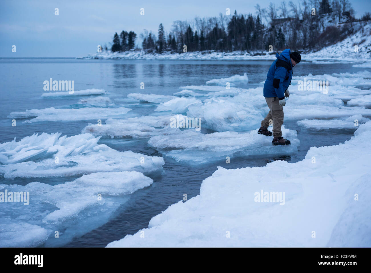 Uomo in cappotto invernale e ganci di trazione sulle fasi stivali su giganteschi blocchi di ghiaccio in movimento fluttuante nel Lago Superiore in inverno Foto Stock