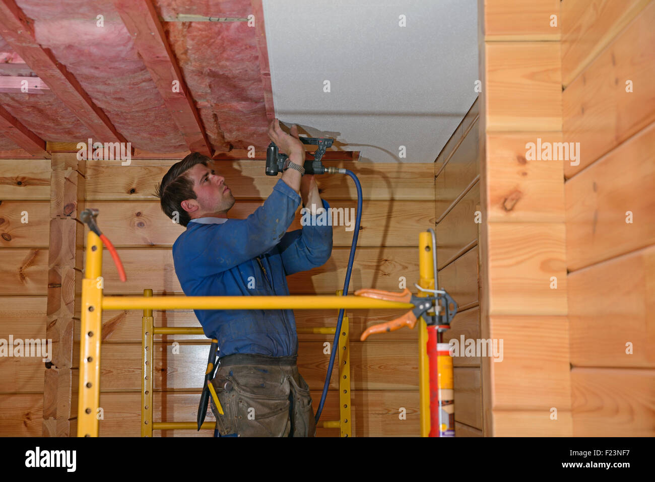 Un Builder consente di eseguire la pinzatura di un massimo di piastrelle da soffitto nel soffitto di un lockwood edificio di stile Foto Stock