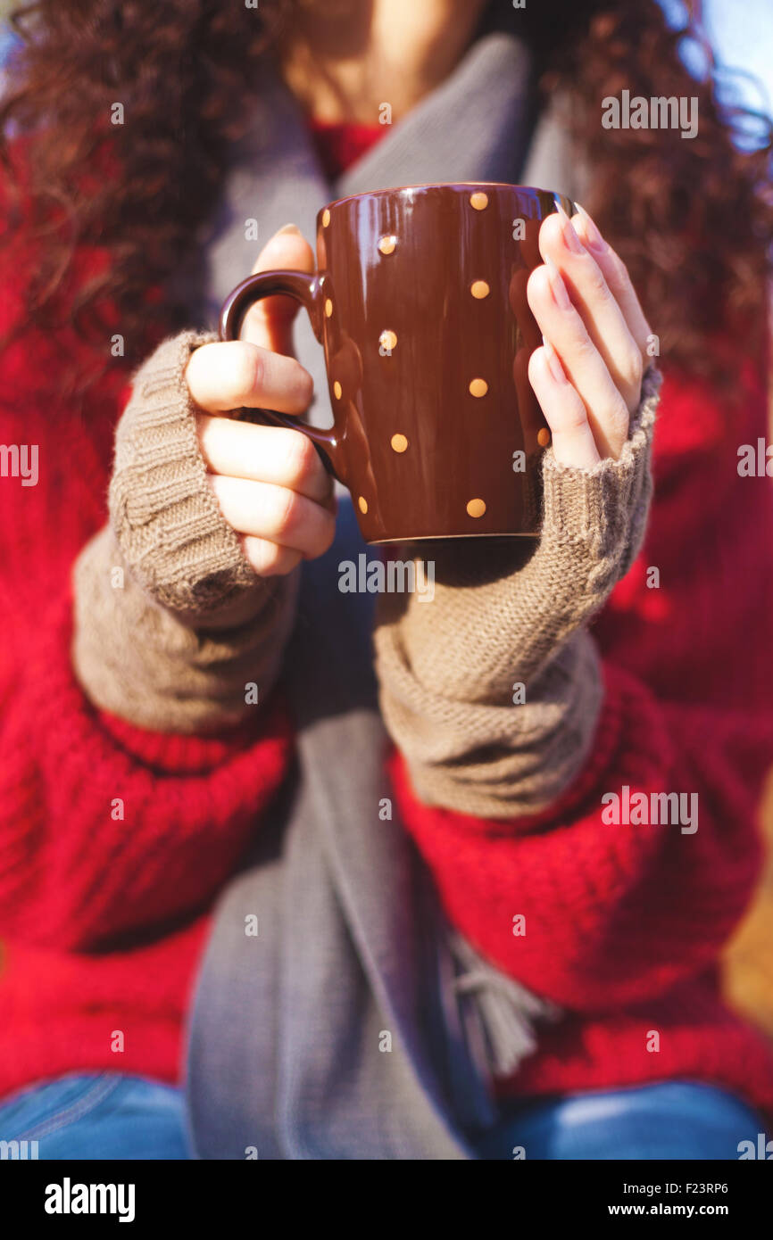 La ragazza di guanti di lana, maglione e sciarpa tenendo una tazza di bevanda Foto Stock