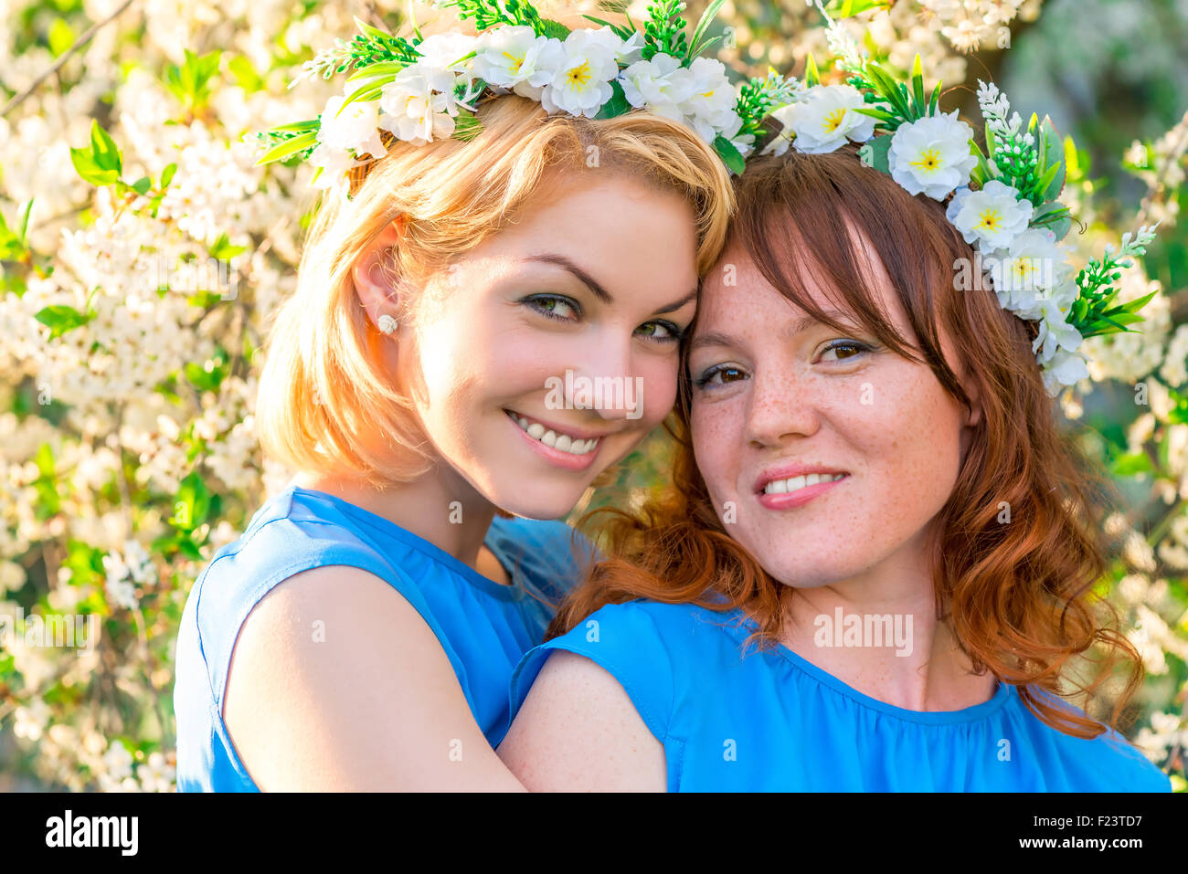 Due amiche con corone di fiori sulla testa vicino alla fioritura cherry nel parco Foto Stock