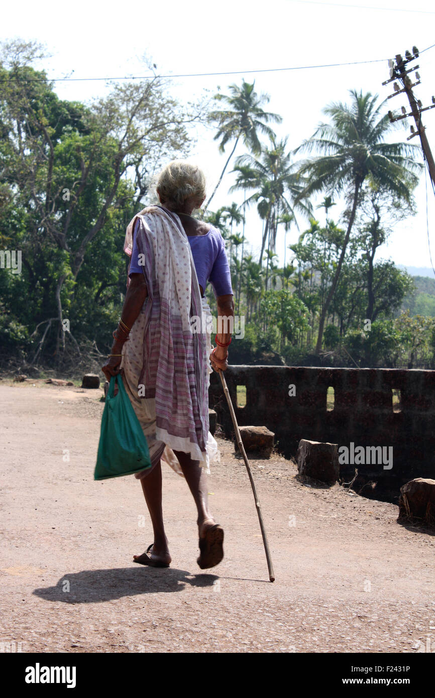 Una vecchia donna da un villaggio indiano, passeggiate con un bastone. Foto Stock