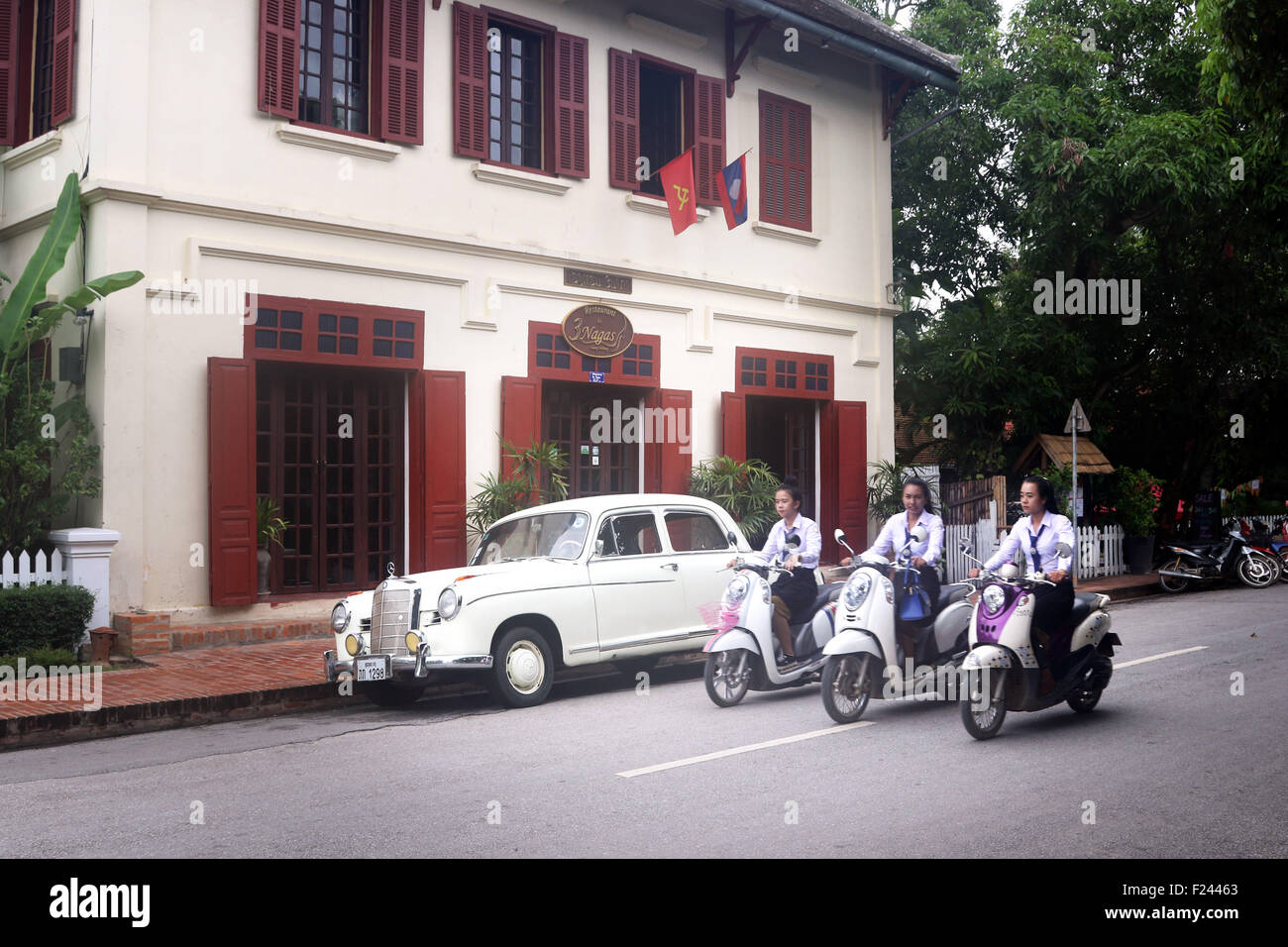Ragazze su scooter passare il vecchio hotel e auto a Luang Prabang città Foto Stock