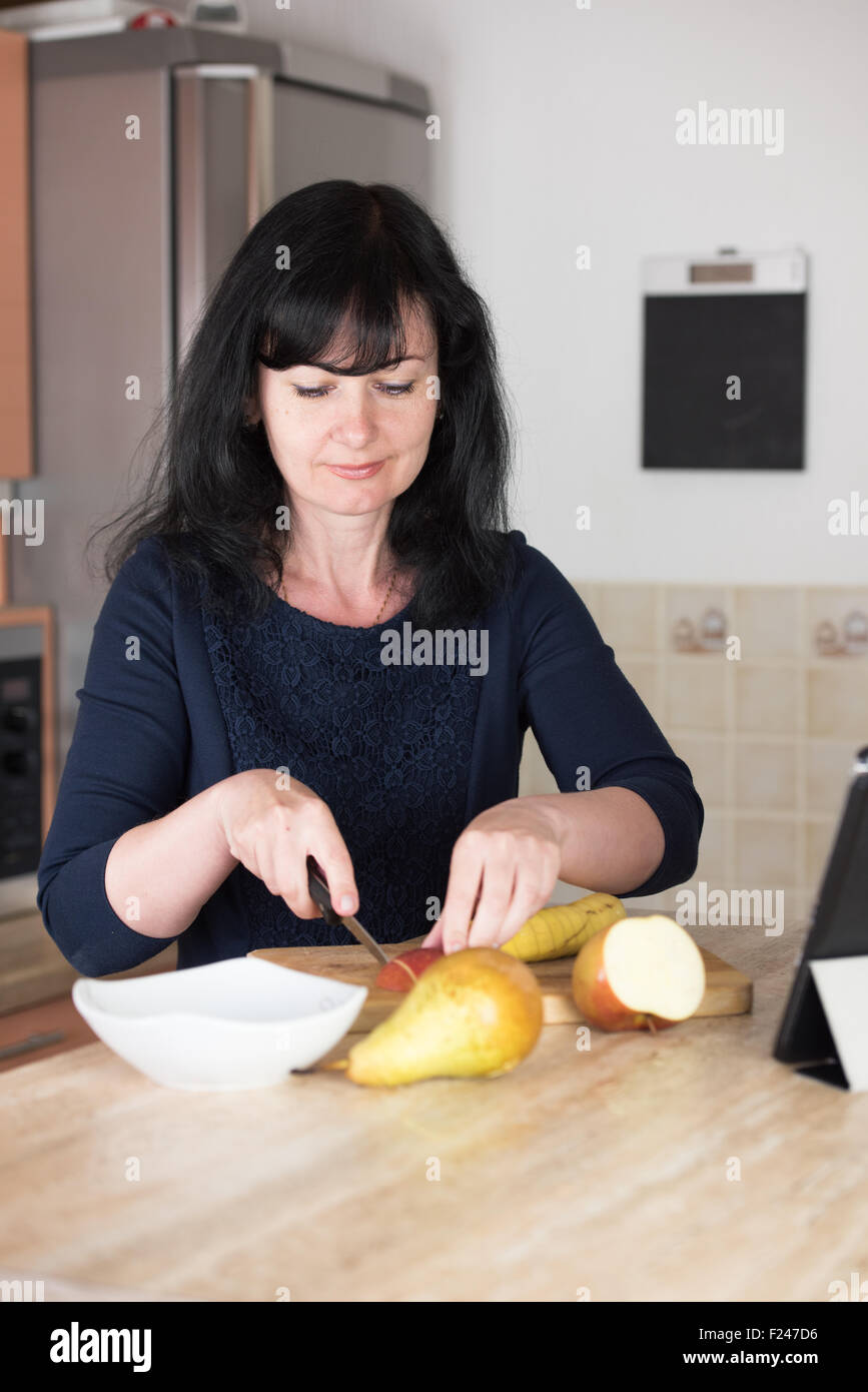 Donna sorridente affettamento apple in cucina sul tagliere per fare un cocktail di frutta Foto Stock Donna sorridente affettamento apple in cucina sul tagliere per fare un cocktail di frutta Foto Stock