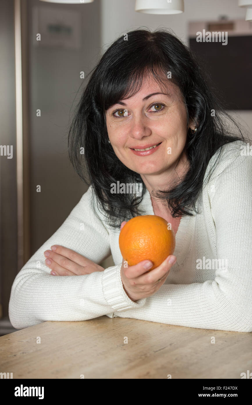 Donna felice tiene un arancione, esaminando la telecamera in cucina Foto Stock