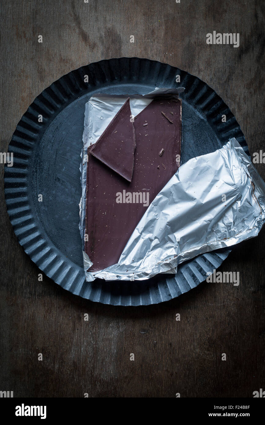 A metà strada scorporato barretta di cioccolato con un pezzo rotto su rustiche latta su sfondo di legno. Vista superiore Foto Stock