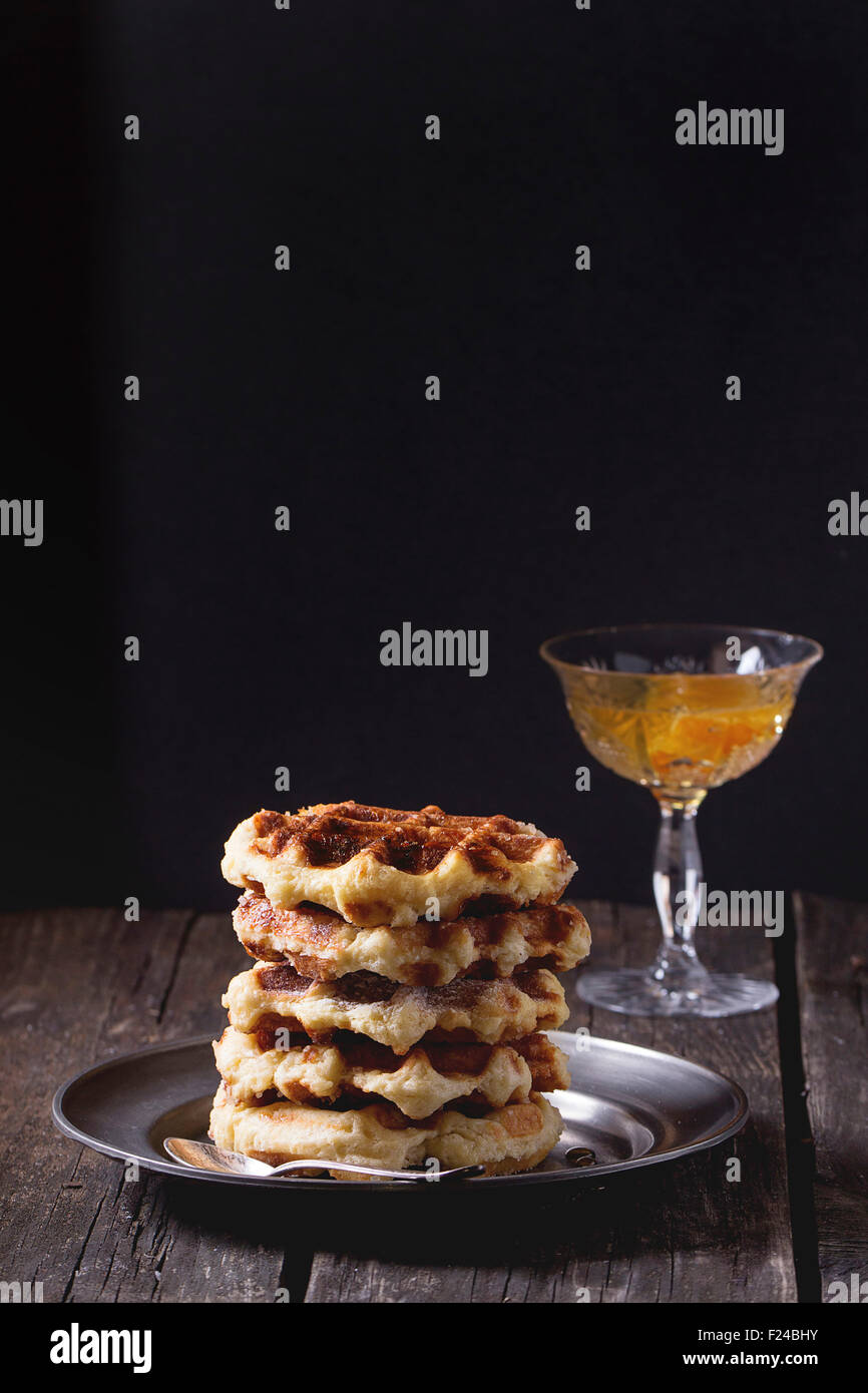 Piastra di metallo con fatti in casa cialde belghe con sciroppo di arancia in vaso a sfondo. Sopra il vecchio tavolo in legno. Scuro in stile rustico. Foto Stock