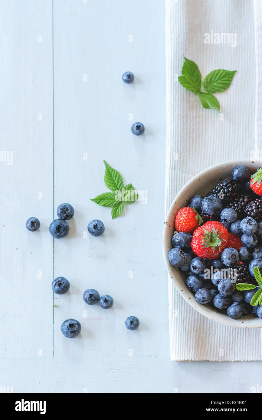 Macchiato il vaso in ceramica con assortimento di bacche mirtilli, fragole e more al tessile bianco tovagliolo in legno tabl Foto Stock