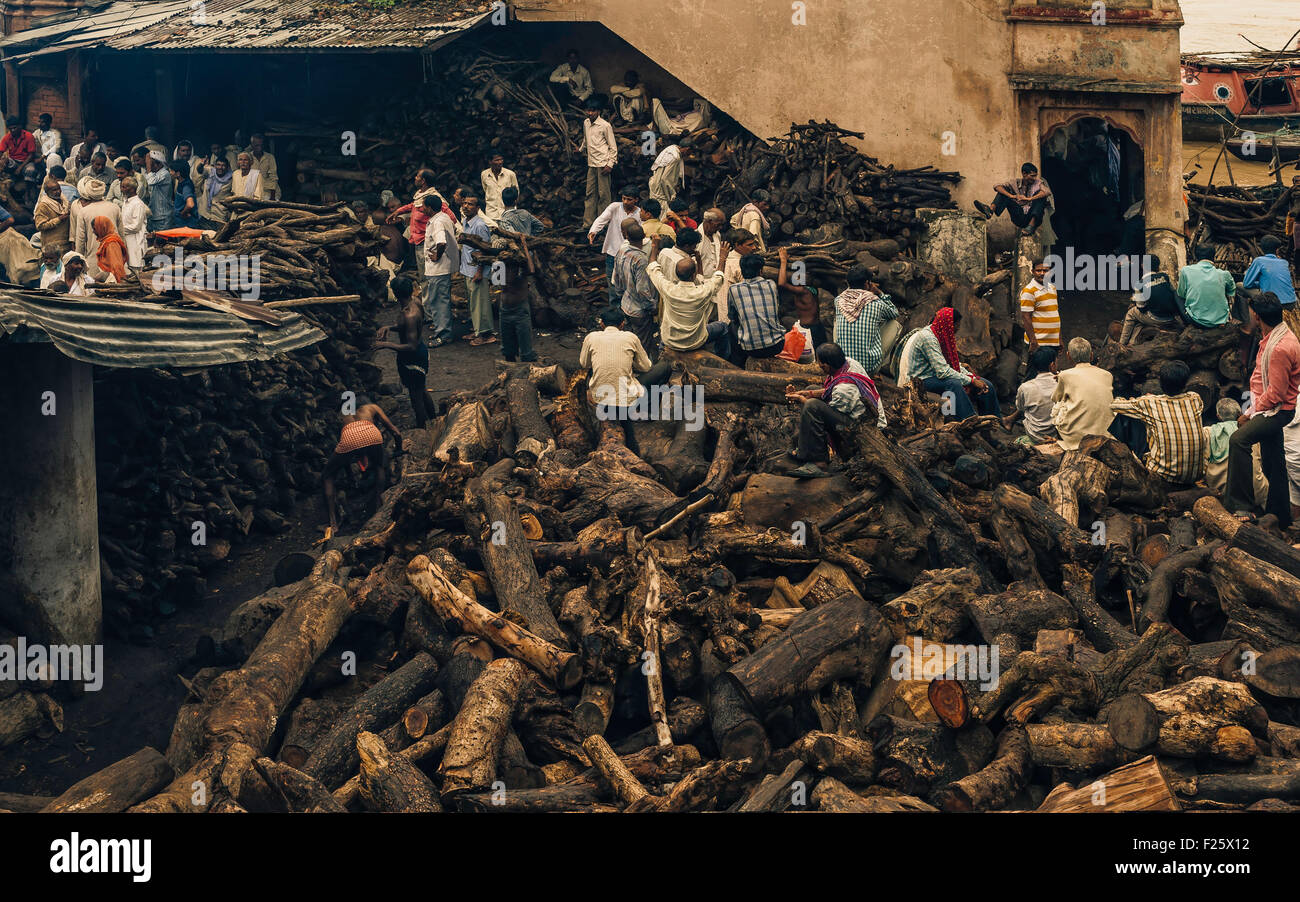 Gli uomini affare a comprare legno per cremazione indù cerimonia in un affollato cortile impilati con legno sulla riva del fiume Gange. Foto Stock