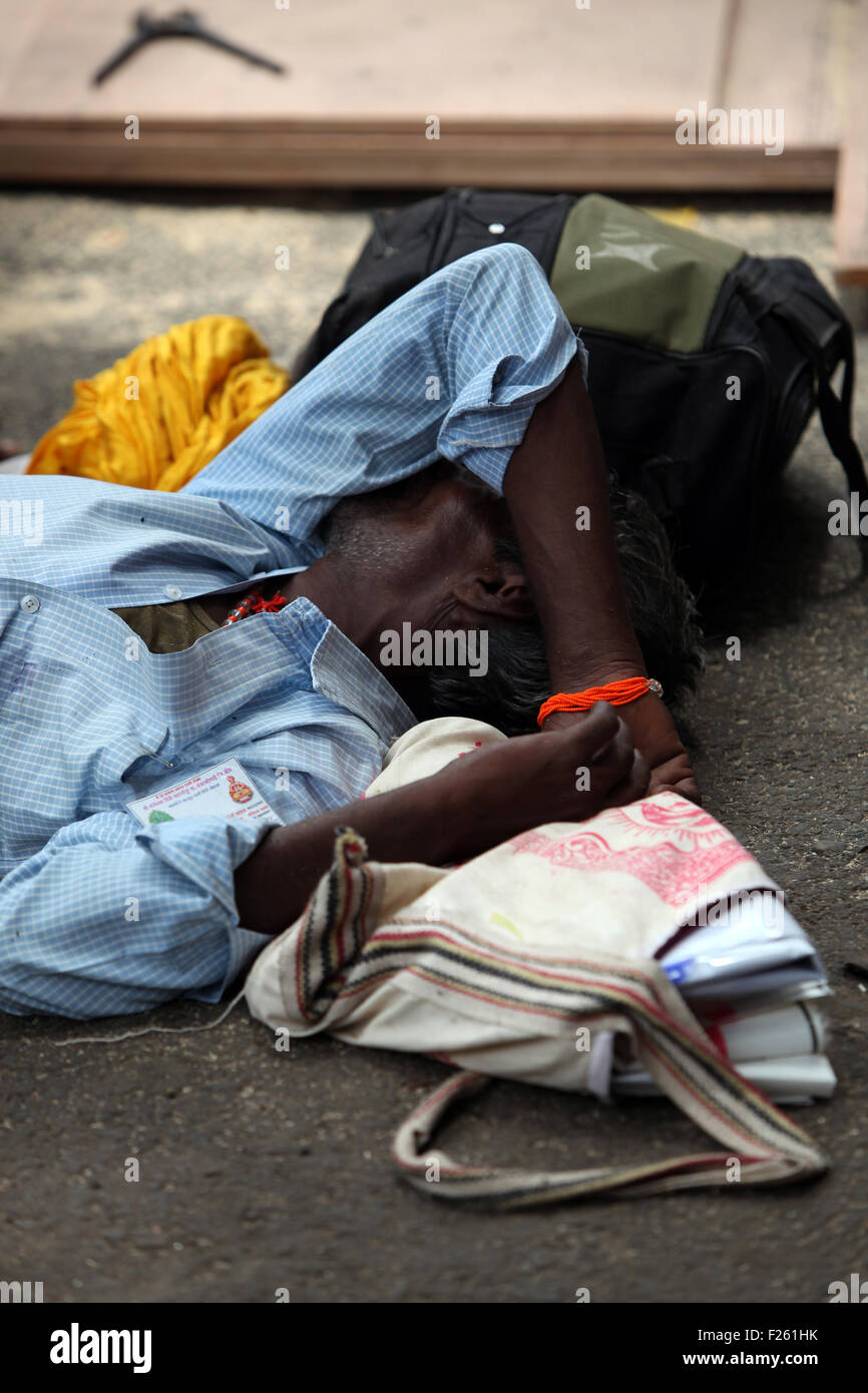 Un povero uomo stanco dorme sul lato di una strada in India. Foto Stock