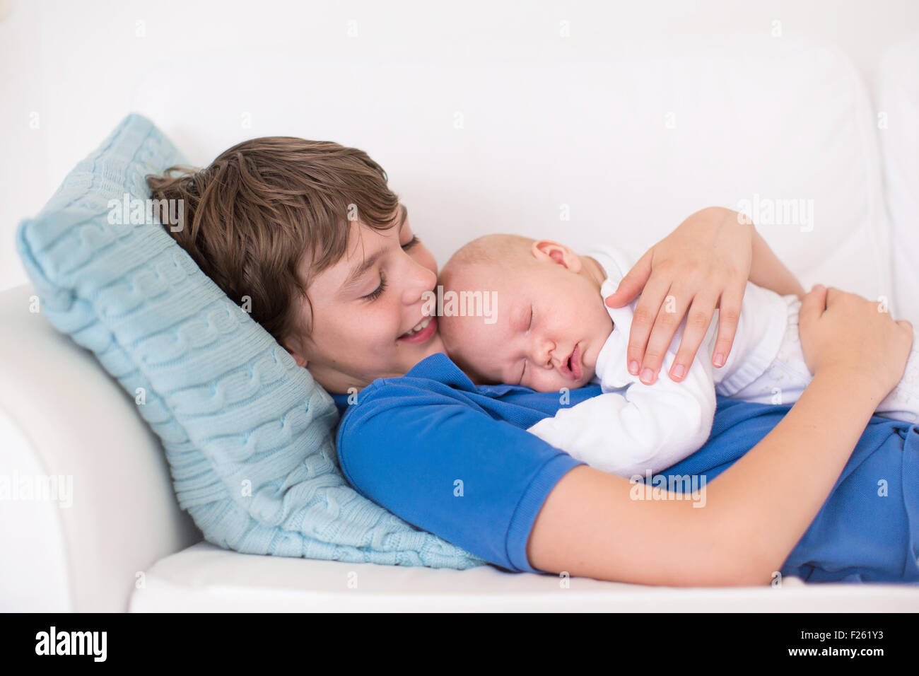Felice di ridere boy tenendo la sua sleeping neonato fratello. Fratelli con grande differenza di età. Bambini che giocano sul lettino bianco Foto Stock