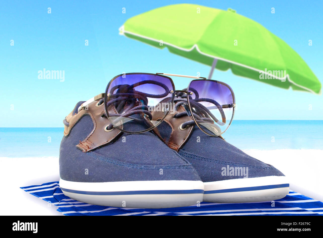Scarpe blu con gli occhiali in appoggio sulla riva sotto un ombrellone con vista sul mare Foto Stock