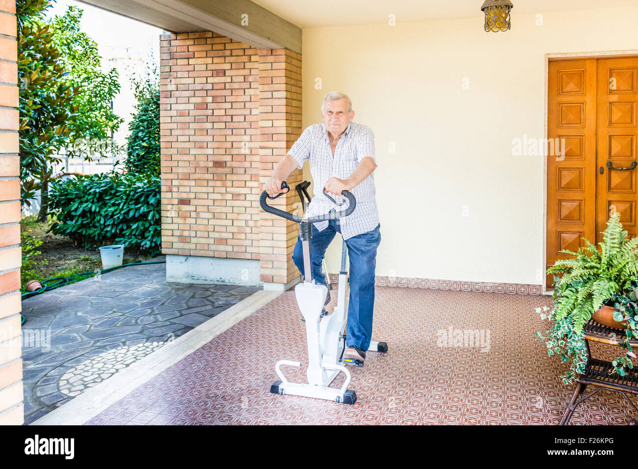 Anziani maschi octogenarian perdere peso rimane montare facendo cyclette sul patio della casa Foto Stock