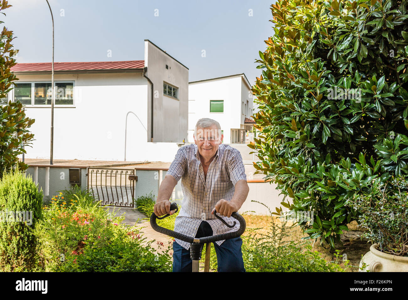 Anziani maschi octogenarian mantiene montare facendo cyclette sul giardino della casa Foto Stock