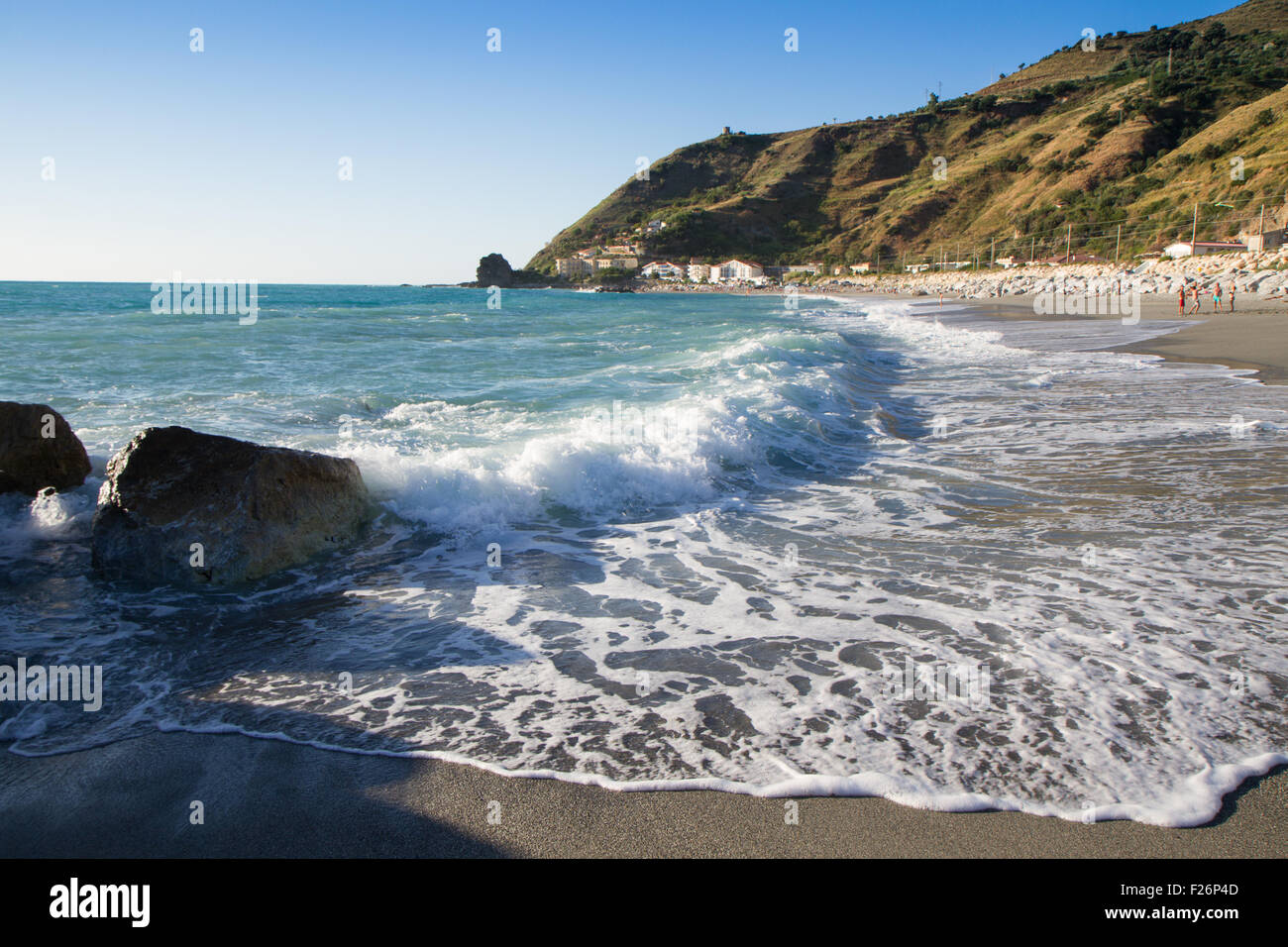 Le onde che si infrangono sulla spiaggia deserta, sullo sfondo azzurro del cielo e delle nubi Foto Stock