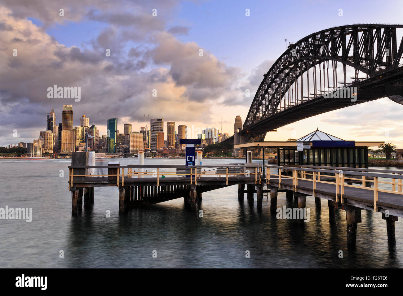 Vista ravvicinata di legno dal molo dei traghetti alla lontana città di Sydney CBD grattacieli e arco di Harbour Bridge, vicino al tramonto Foto Stock