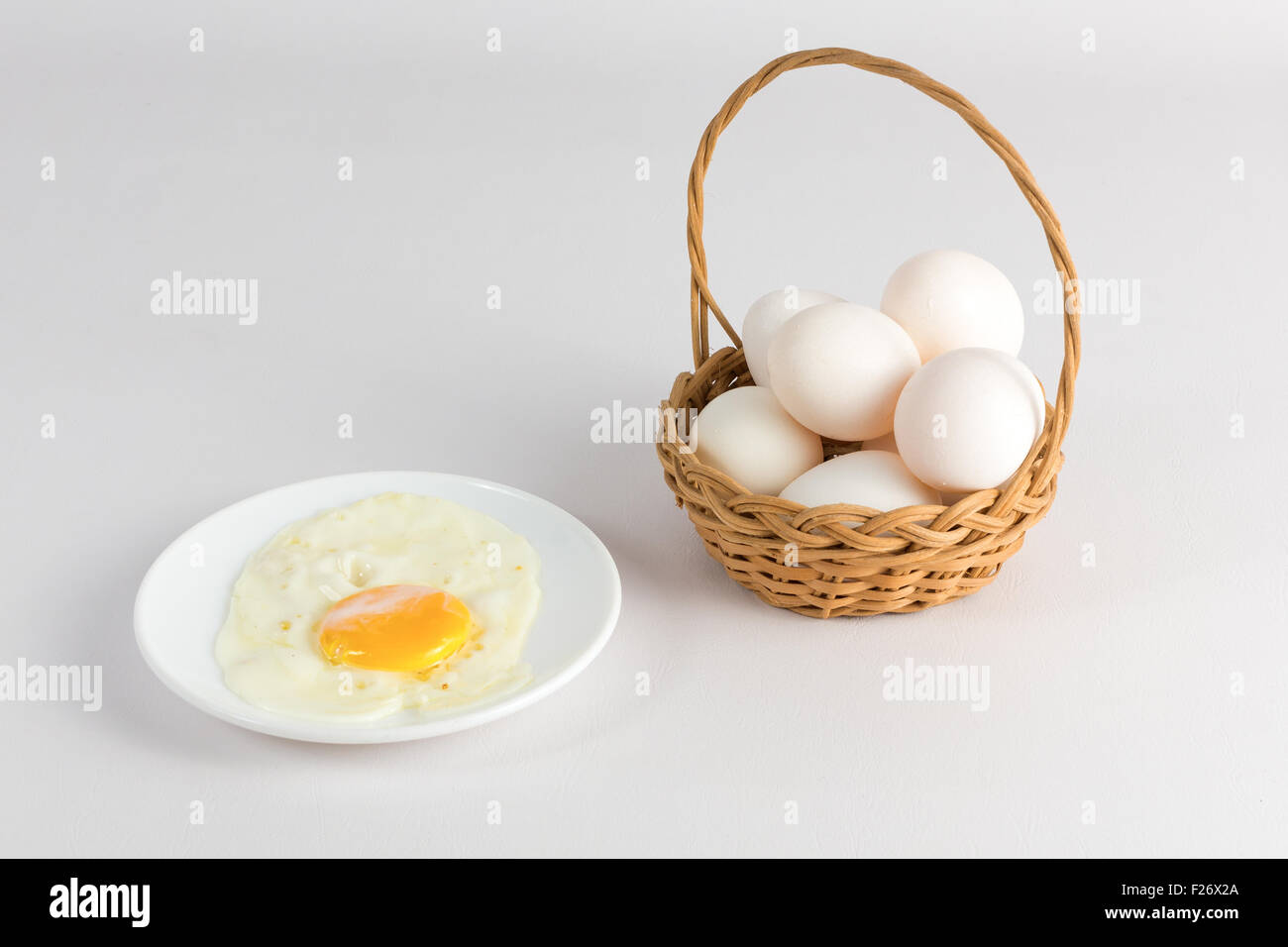 Fritti di uova di gallina in un piatto bianco e un cesto con uova Foto Stock