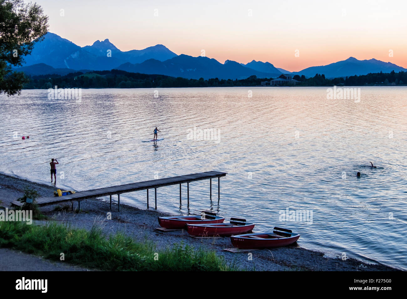 Alpi bavaresi, tramonto , nuotatori e paddle-sciatore in Forggensee lake, Ostallgaü, Baviera, Germania Foto Stock