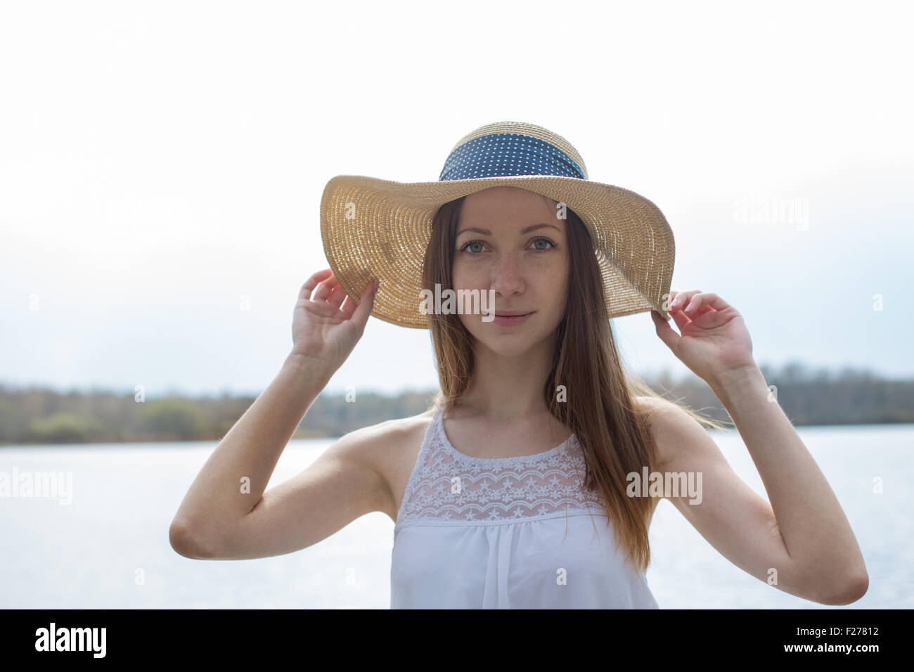 Freckled felice ragazza in abito bianco azienda cappello di paglia e guardando la fotocamera in tempo ventoso Foto Stock
