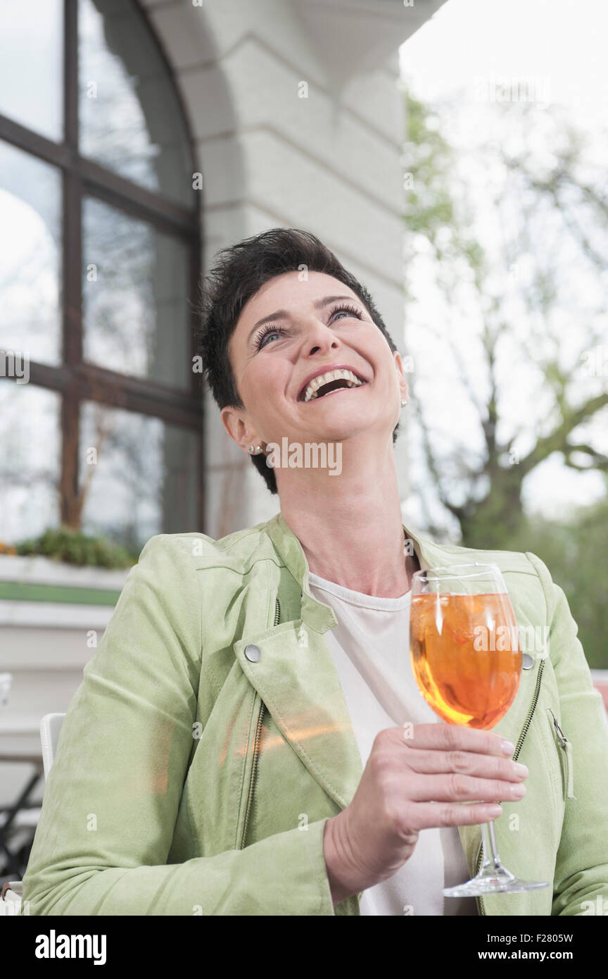 Donna matura a ridere con aperol spritzat al cafè sul marciapiede, Baviera, Germania Foto Stock