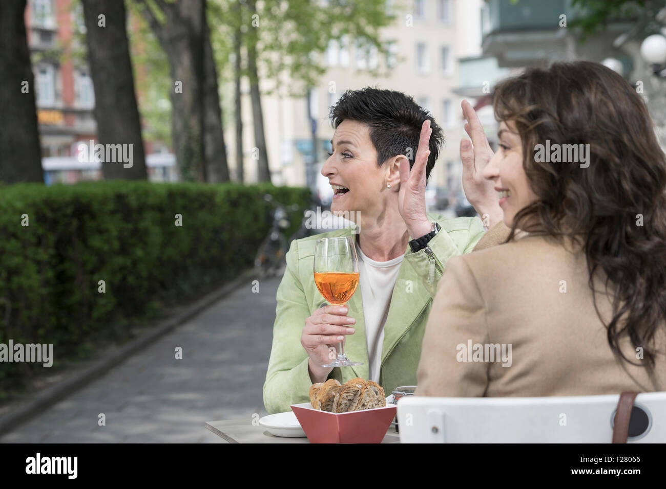 Due amici agitando la mano al cafè sul marciapiede, Baviera, Germania Foto Stock