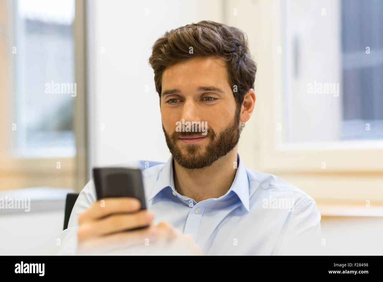 Allegro uomo barbuto con il suo smartphone in un ufficio moderno Foto Stock