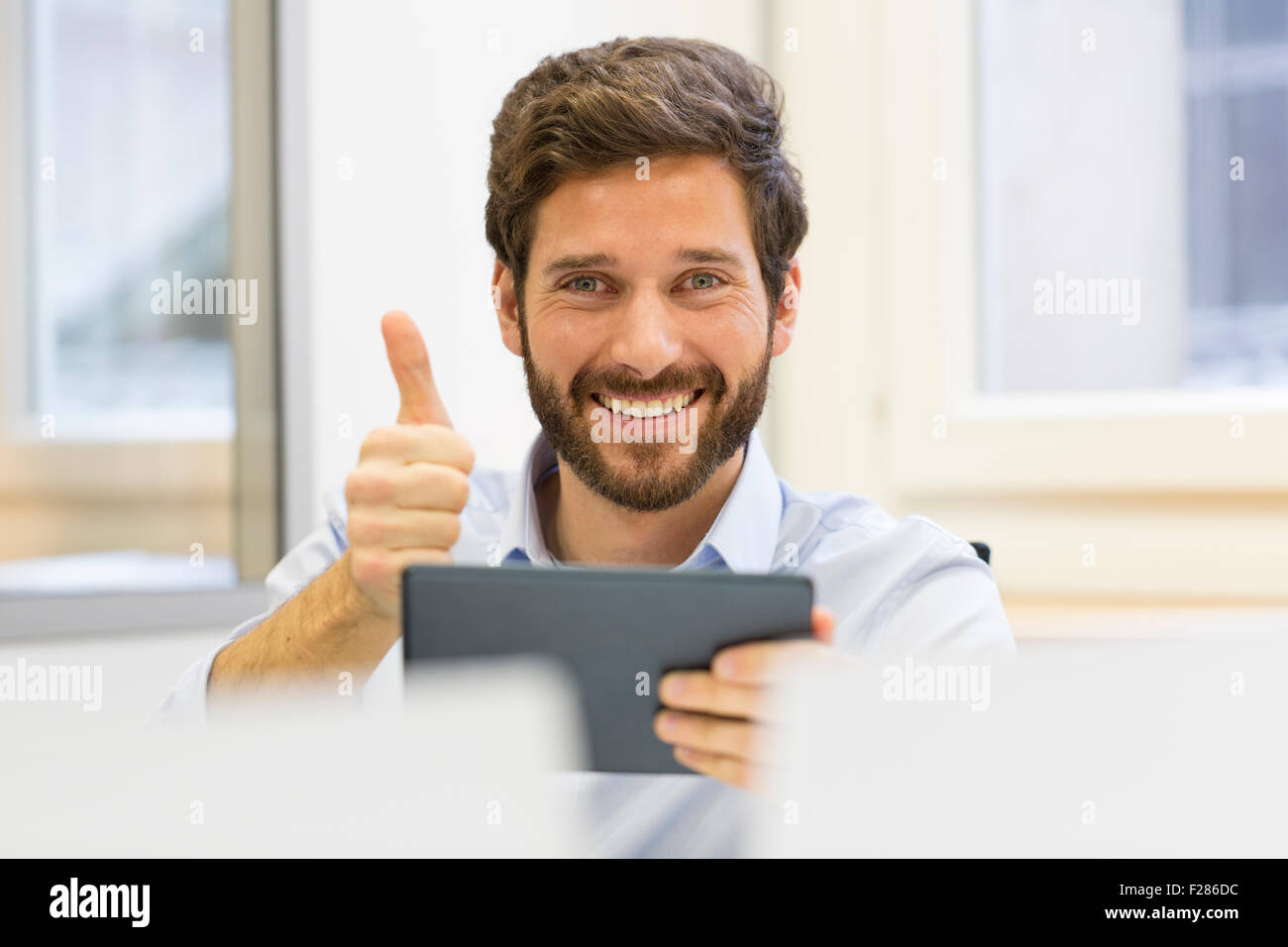 Happy businessman con il pollice in su in ufficio utilizzando tavoletta digitale Foto Stock