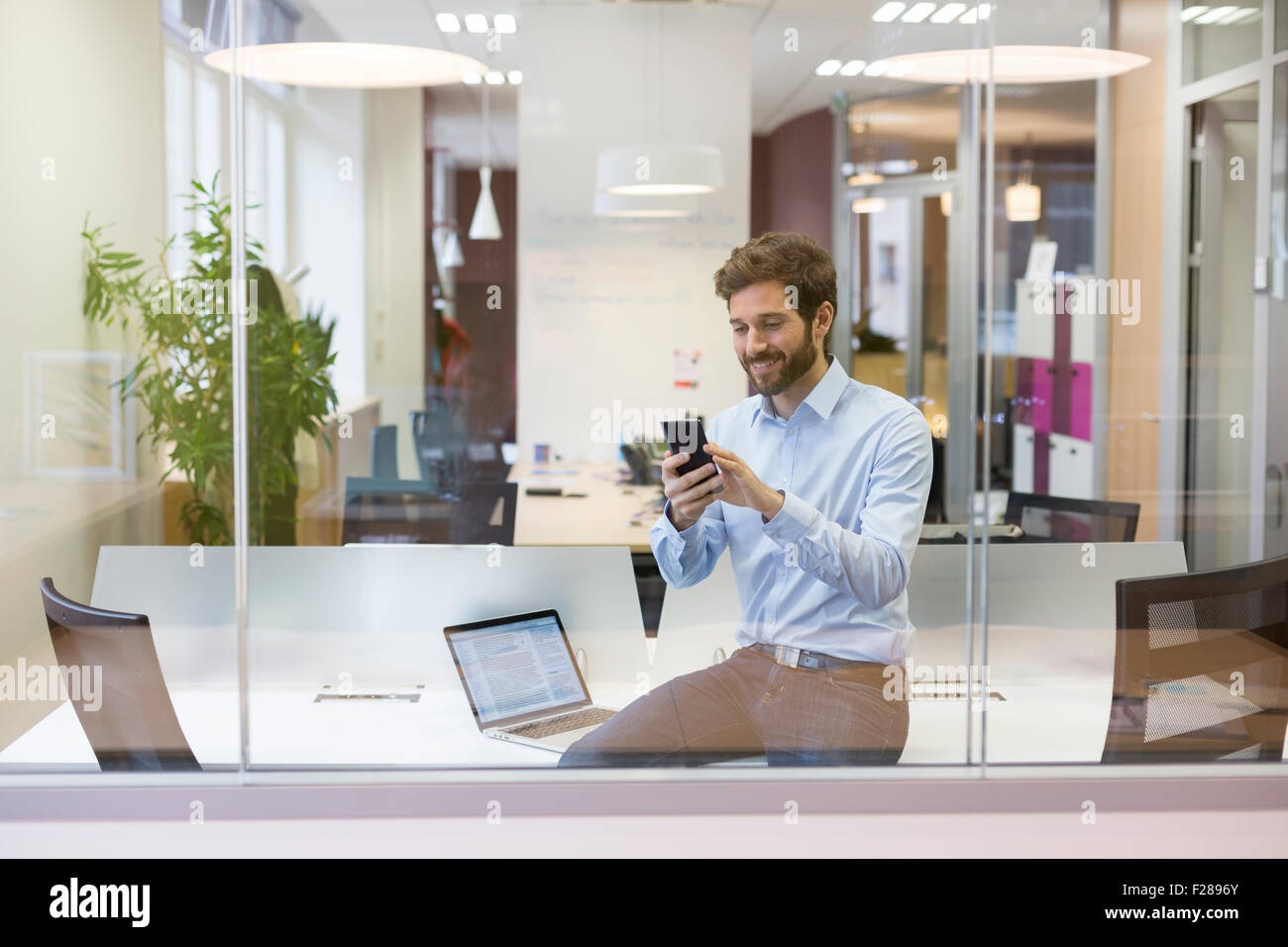 Hipster uomo informale. La digitazione di un messaggio di testo sul telefono cellulare in open space office Foto Stock