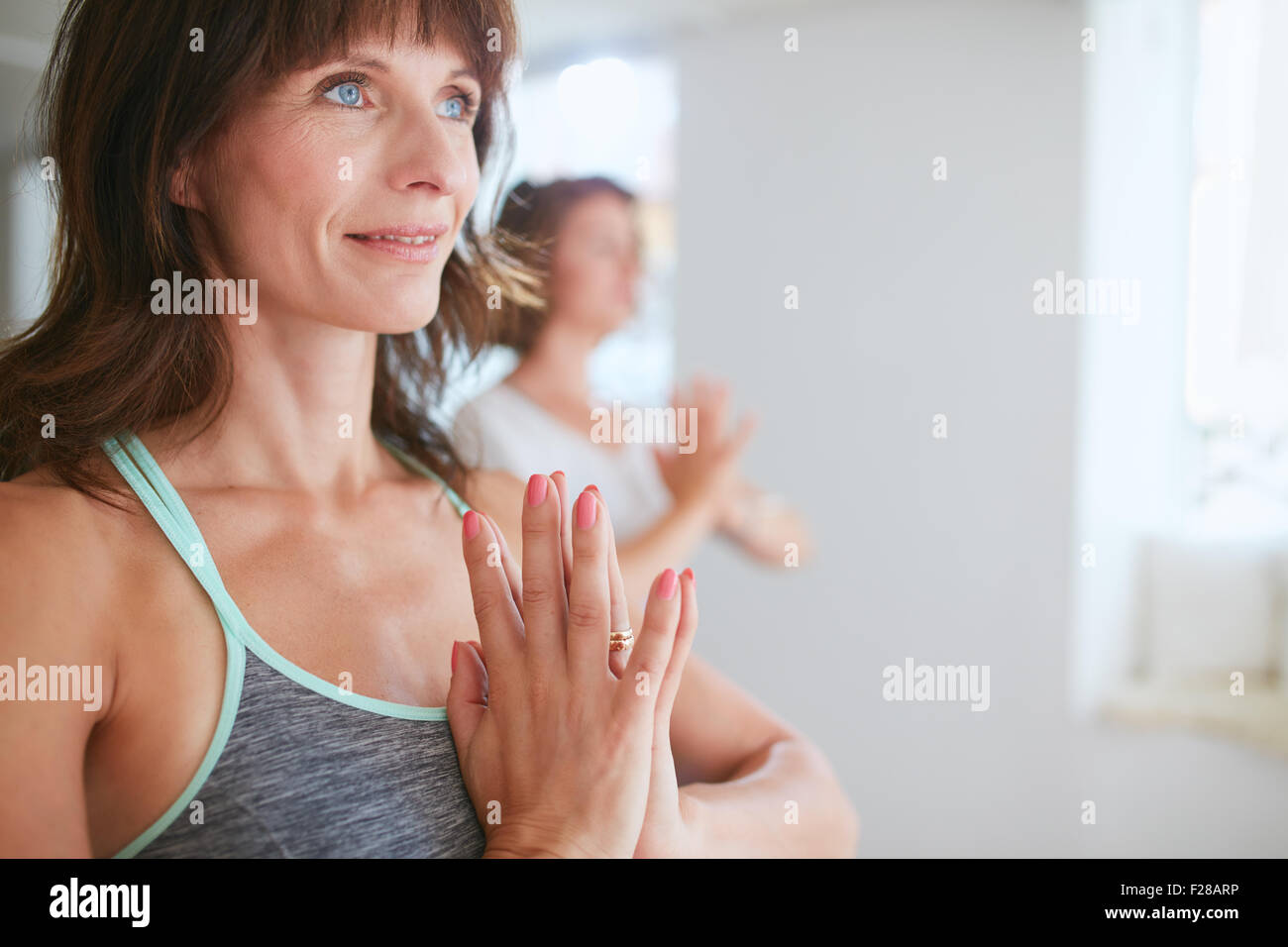 Immagine ravvicinata di felice donna matura fare yoga che guarda lontano sorridente. Le donne in posa yoga vrikshasana utilizzando Namaste. Foto Stock
