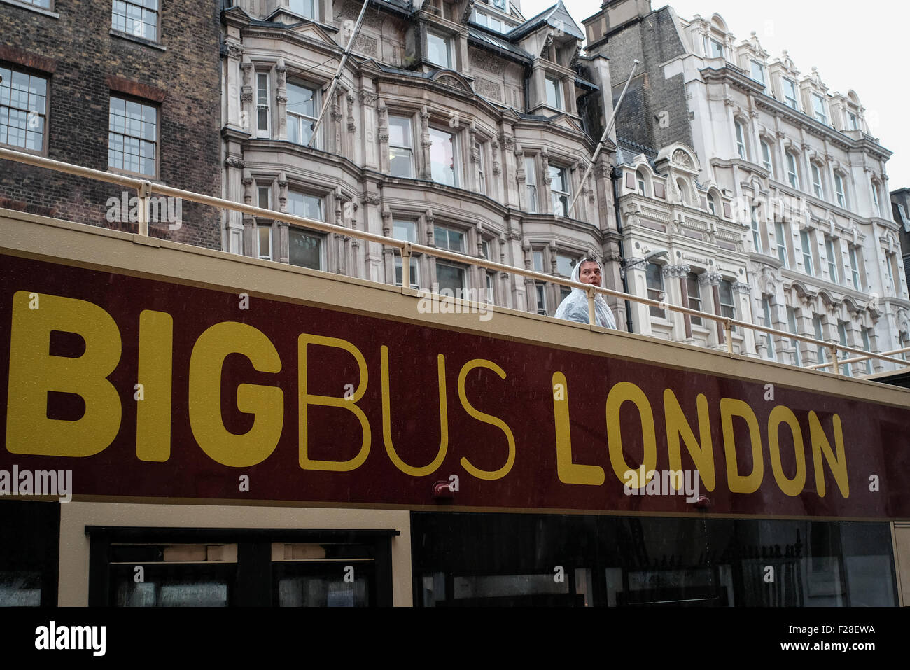 Un uomo si erge una solitaria figura sulla parte superiore di una apertura di autobus di Londra sotto la pioggia che indossa una pioggia di mac Foto Stock