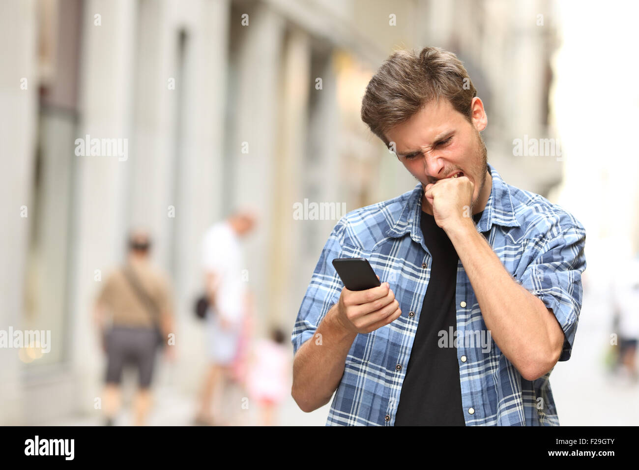 Furious angry man guardando le applicazioni nel telefono cellulare in strada Foto Stock