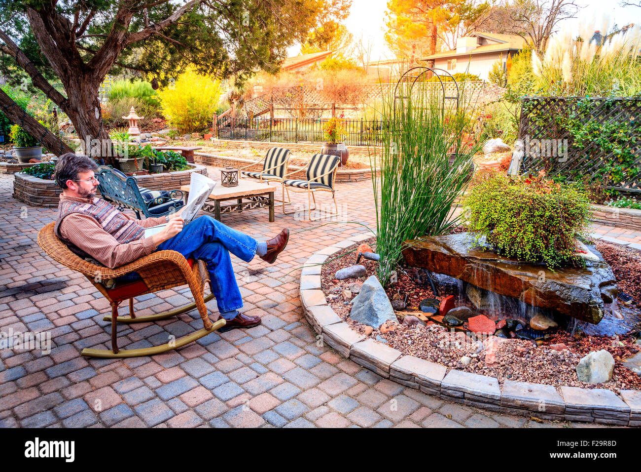 L uomo è la lettura di un giornale su un patio in un accogliente giardino Foto Stock