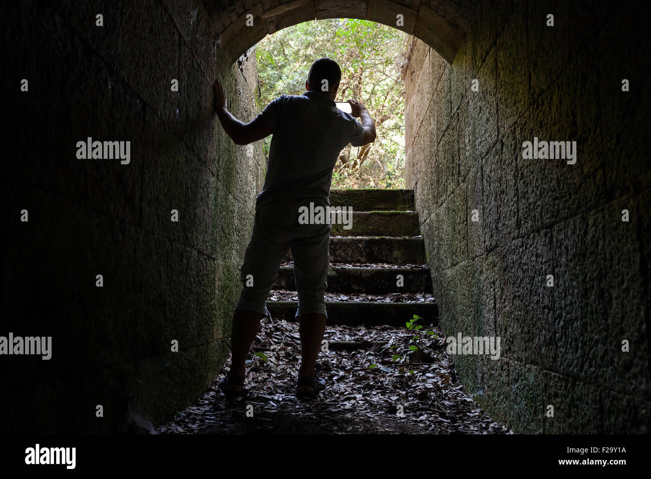 Giovane uomo è tenuto foto sul suo telefono cellulare dal buio del tunnel di pietra Foto Stock