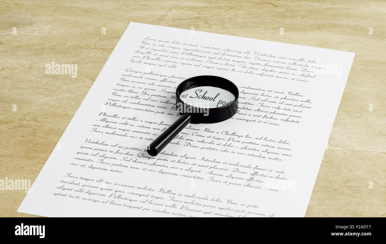 Lente di ingrandimento Ingrandimento la parola scuola su una pagina con il testo stampato recante su di un desktop Foto Stock