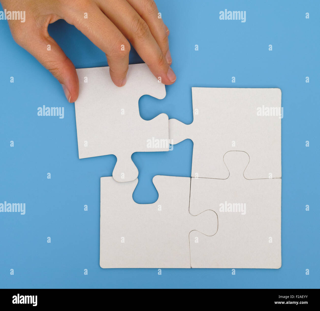 Donna mettendo a mano il pezzo finale per completare semplice puzzle su sfondo blu Foto Stock
