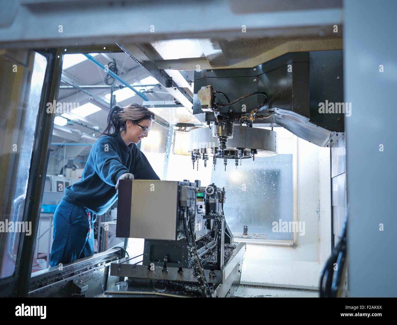 Femmina ingegnere apprendista impostazione tornio CNC in fabbrica di ingegneria Foto Stock