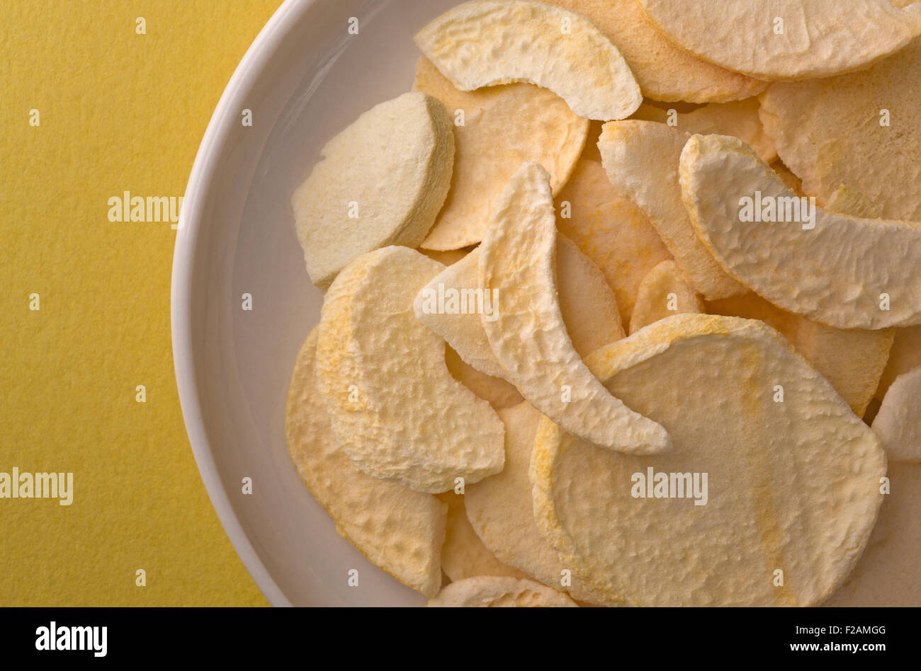 Top vista ravvicinata di pesche secche le fette su un piatto in cima a un giallo tavolo illuminato con luce della finestra. Foto Stock