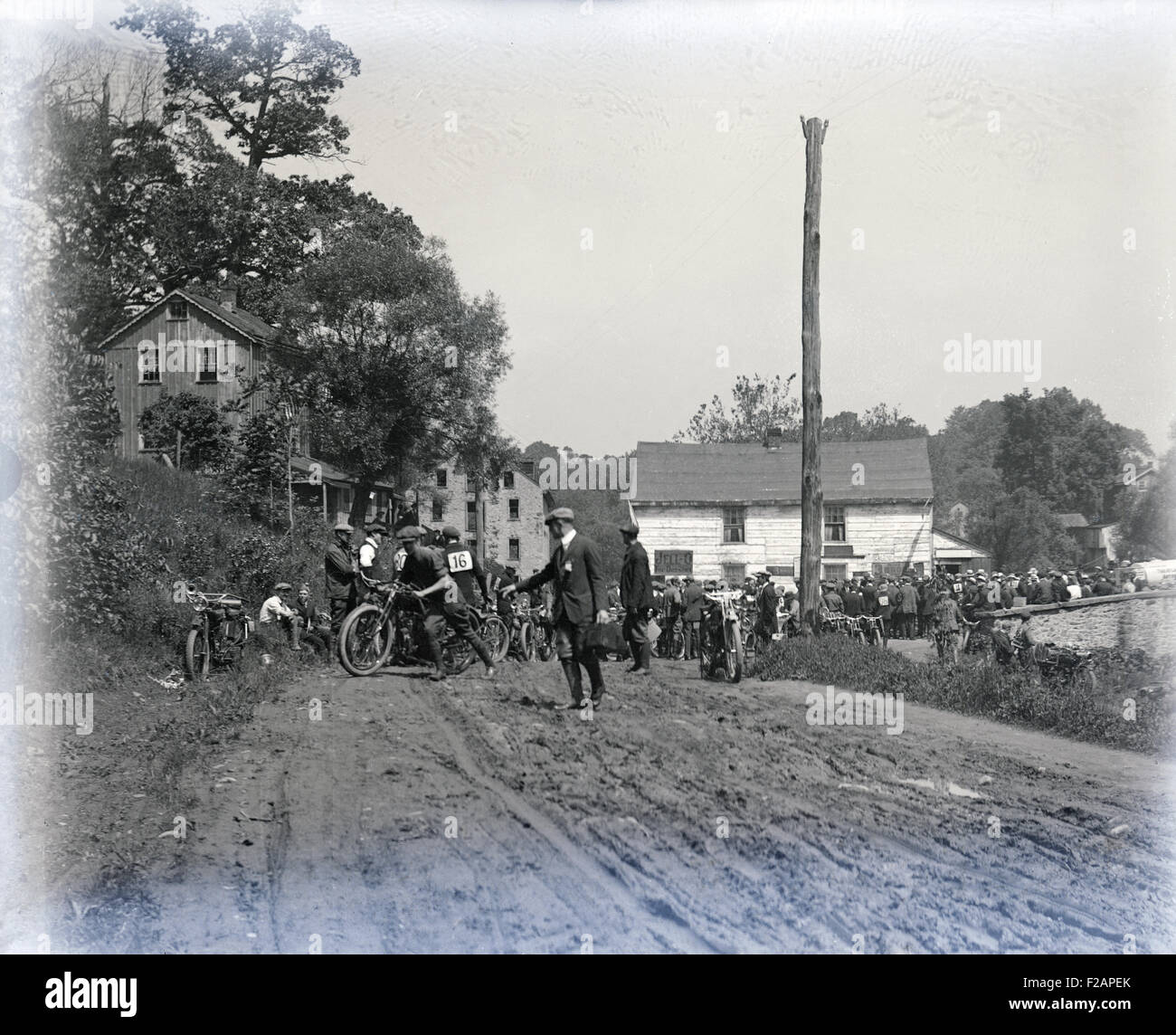 Antico risalente al 1910 fotografia, i partecipanti in un inizio di gara di moto in una piccola città con strade fangose. Posizione, STATI UNITI D'AMERICA. Foto Stock