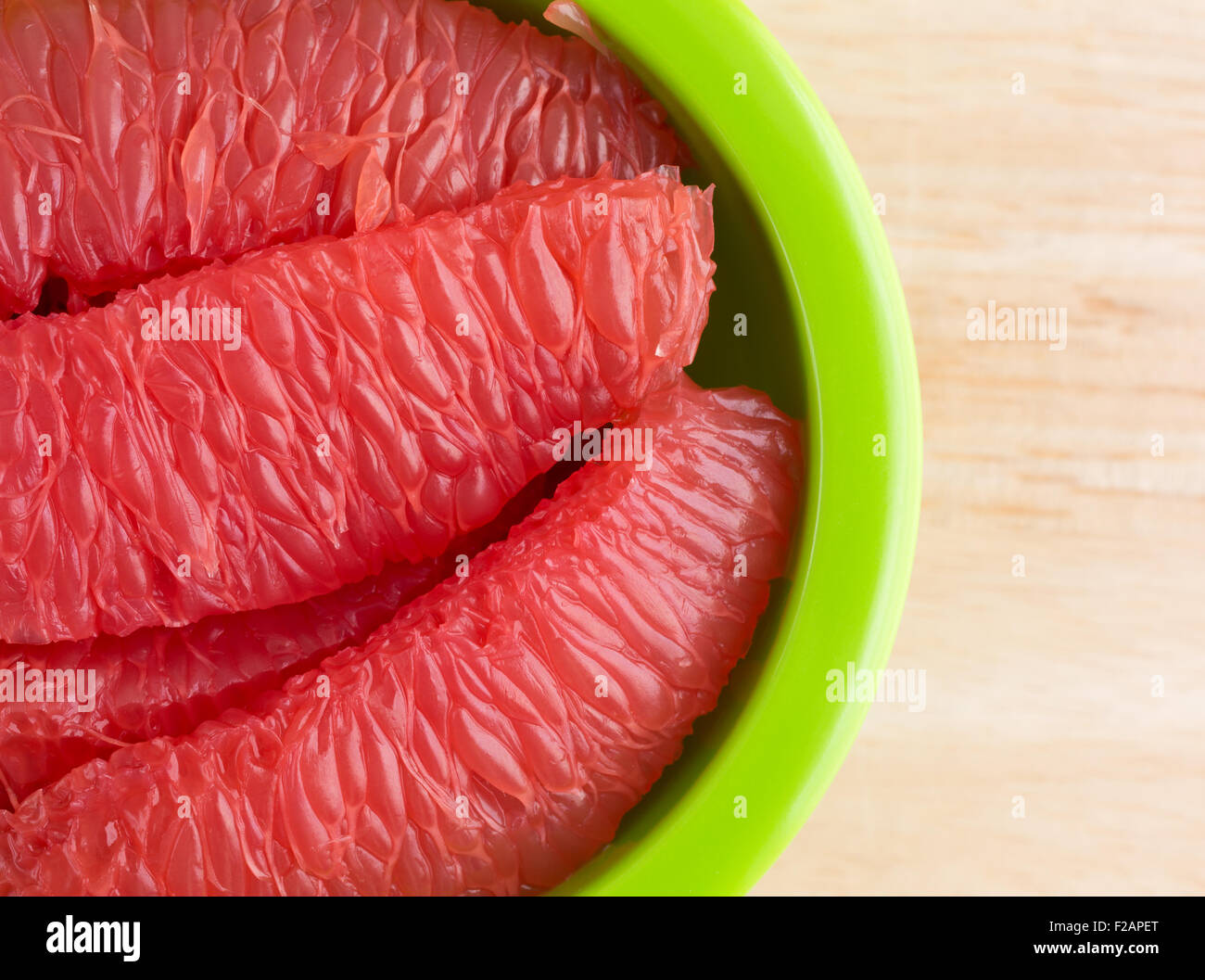 Parte superiore in prossimità delle sezioni di pompelmo rosso in una ciotola verde su una tavola di legno alto. Foto Stock