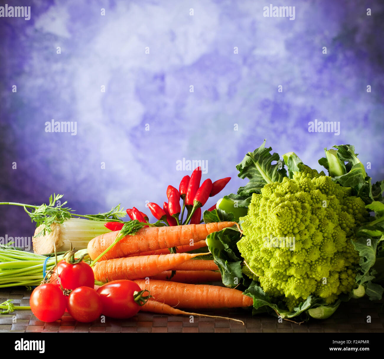 Cavolo romano, carote, pomodori e altri ortaggi su sfondo viola Foto Stock